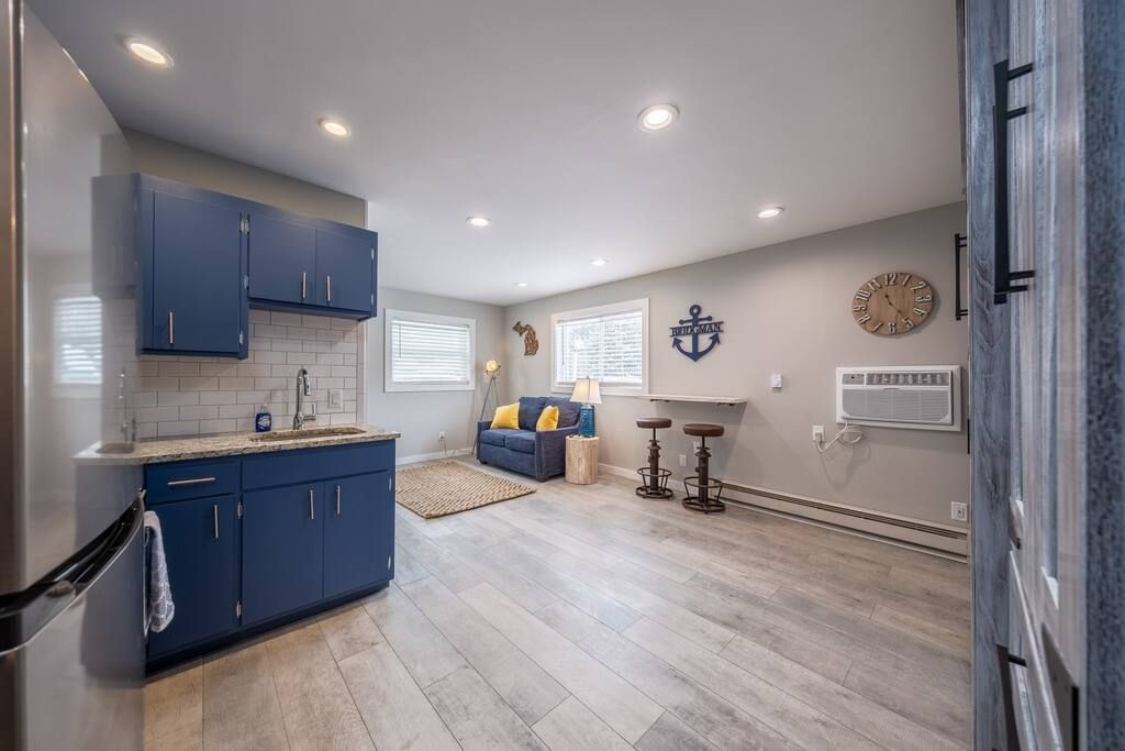 A kitchen with blue cabinets , a refrigerator , a sink , and a couch.