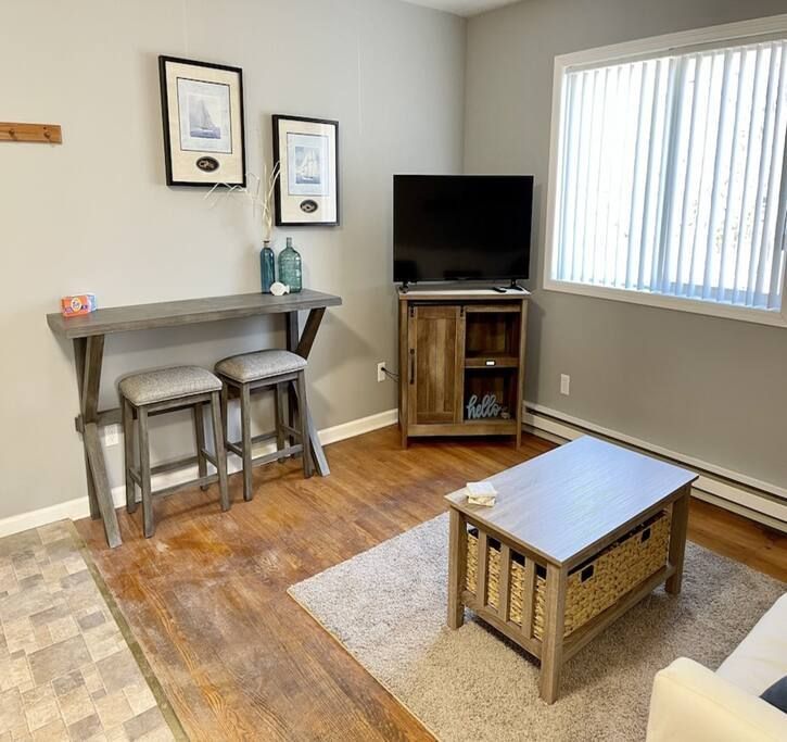 A living room with a couch , table , stools and a flat screen tv.