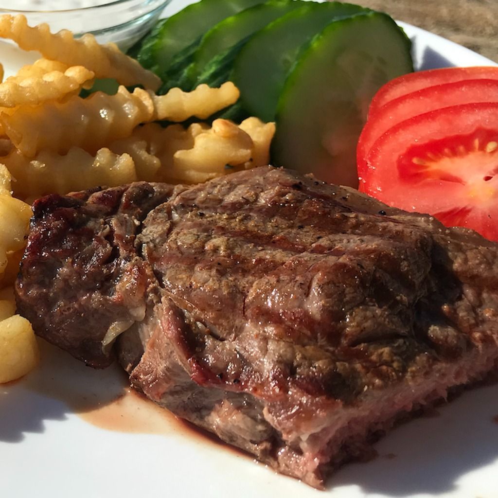 Steak with fries, tomato slices, cucumber, and sauce on a white plate.