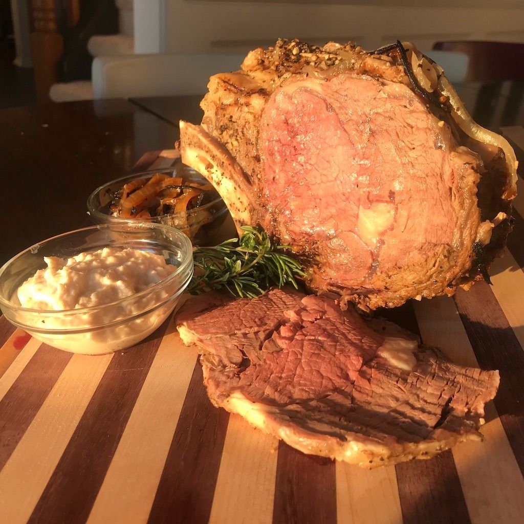 Roasted prime rib with sides, on a wooden cutting board.