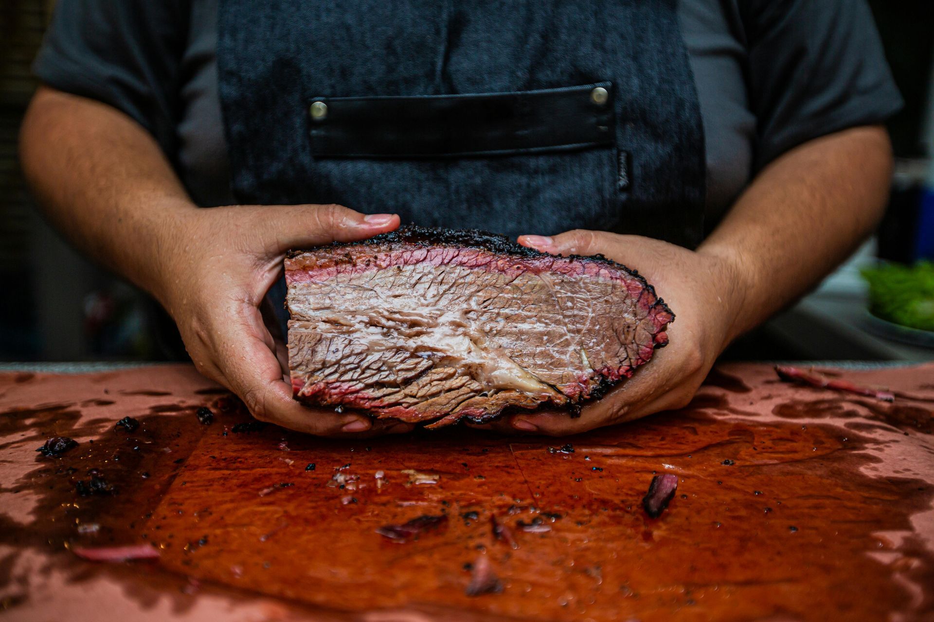 Person holding a sliced brisket, showing the meat's texture and smoke ring. On a wooden cutting board.