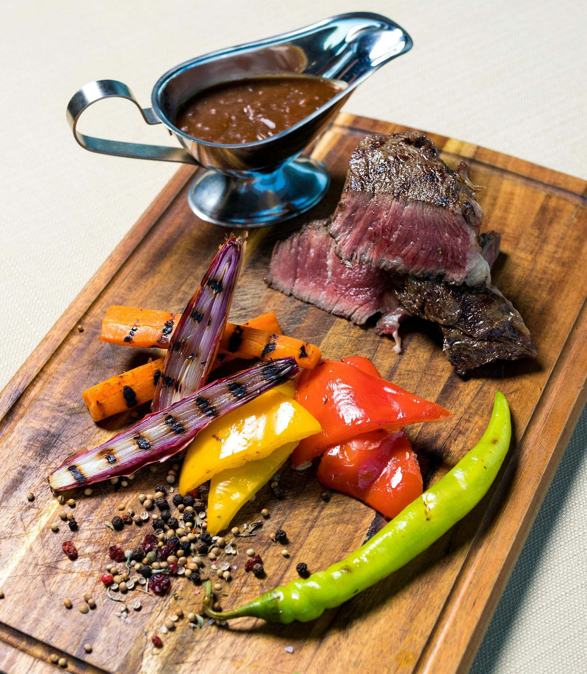 Steak with grilled vegetables, gravy, on a wooden board.