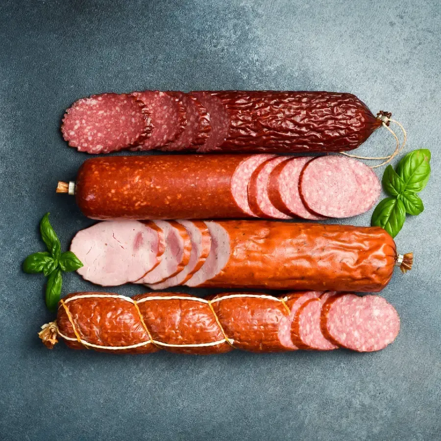 Four types of sliced sausage on a gray surface, with fresh basil leaves.