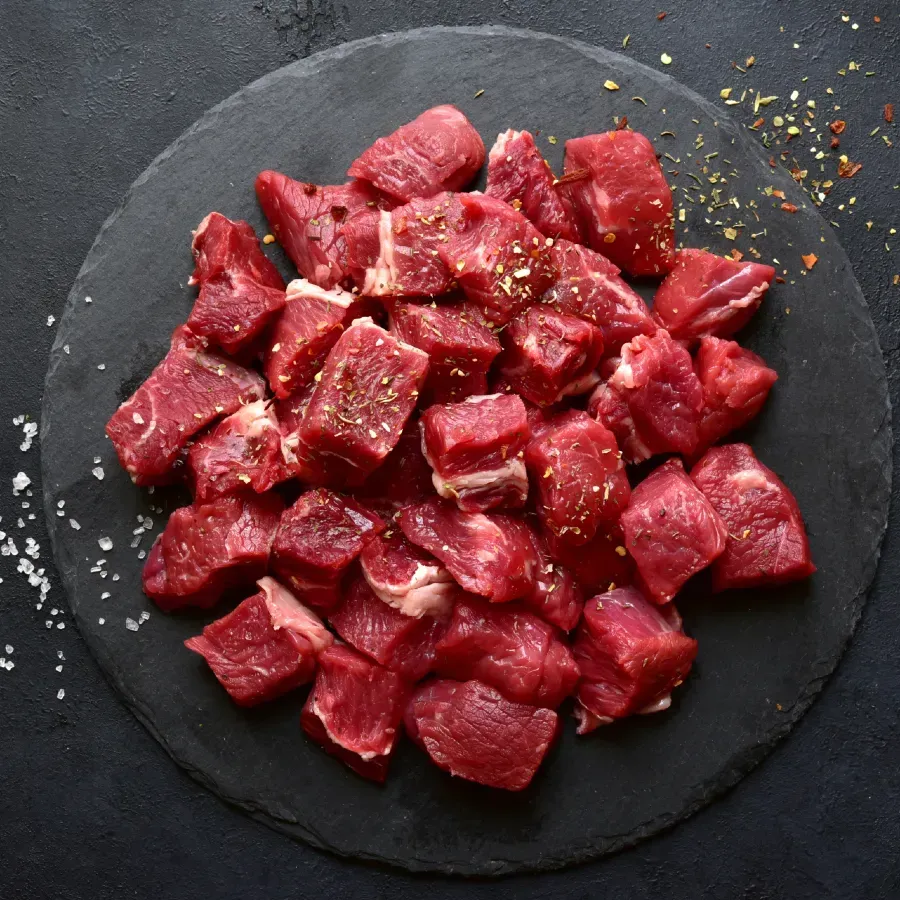 Diced raw beef cubes on a black slate, seasoned with herbs and spices.