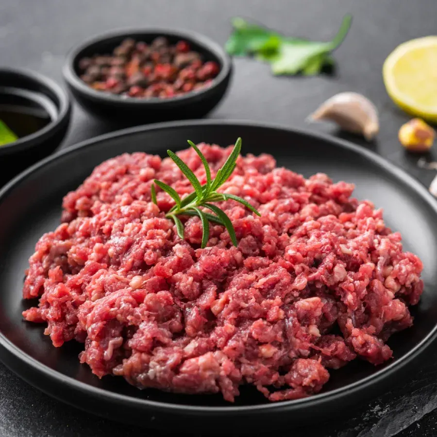 Raw ground meat on a black plate, garnished with rosemary.