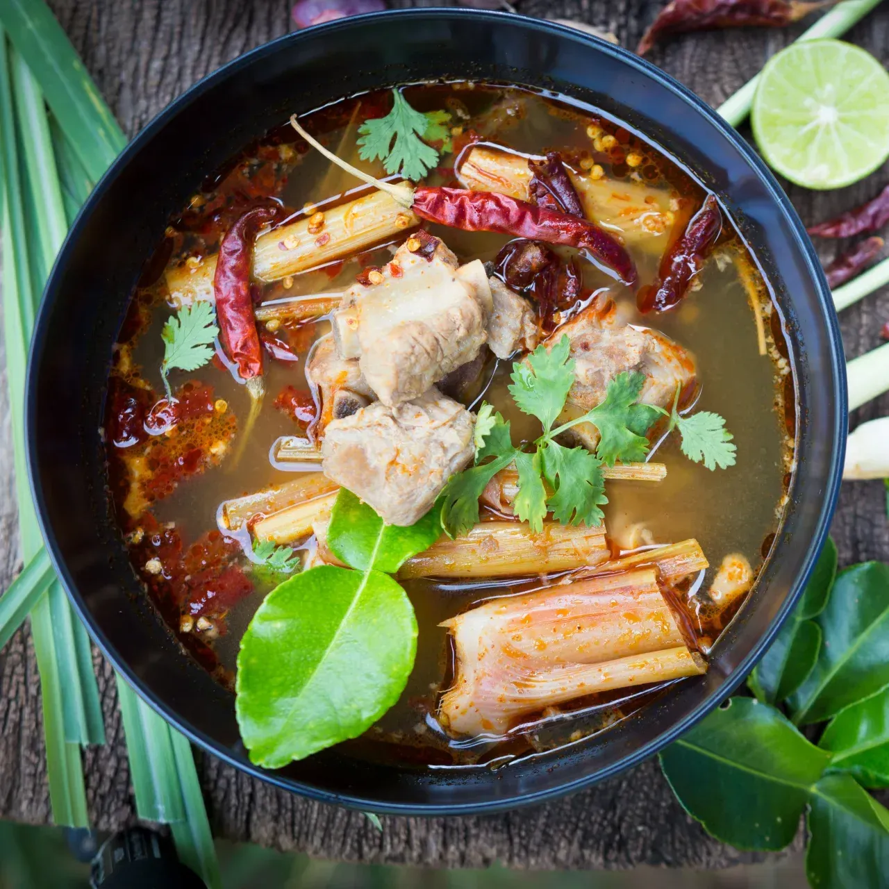 Bowl of Tom Yum soup with pork, chili peppers, and herbs.