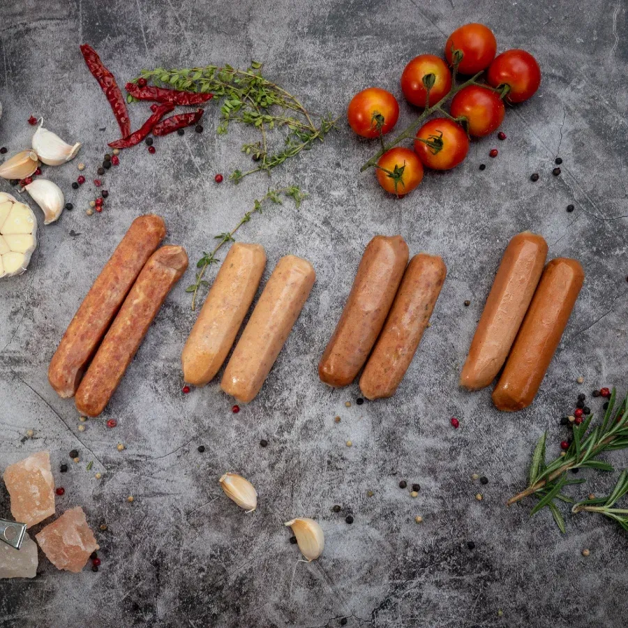 Sausages arranged with fresh tomatoes, herbs, garlic, chili peppers, salt on a gray surface.