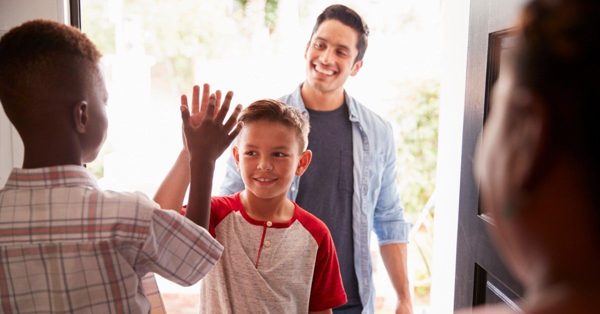 Two pre-teen boys high-fiving each other in the open doorway as the dad, behind his son, smiles at them.