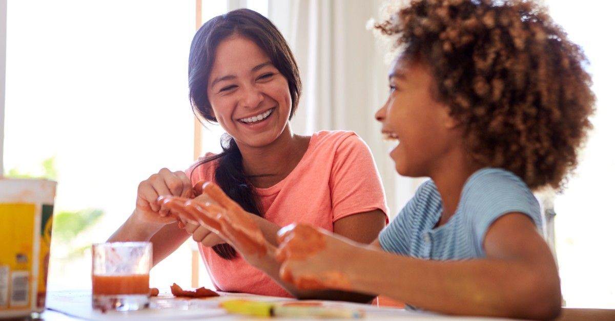 Two pre-teen girls laughing and smiling at a table doing arts and crafts. They're playing with slime or modeling clay.