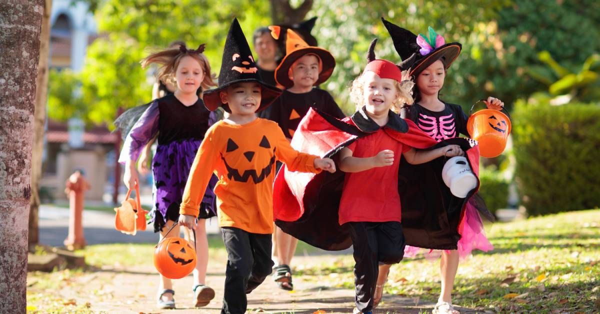 A group of children in different Halloween costumes running and trick or treating in a residential neighborhood.