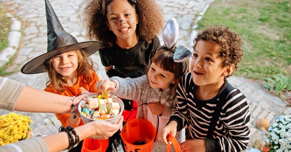 Four children in various Halloween costumes, trick or treating and grabbing candy out of a small bowl.