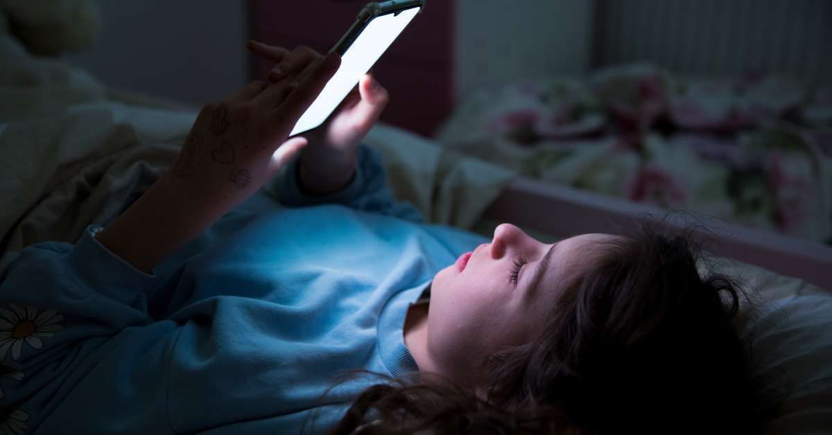 A child using a phone lying in bed late at night while scrolling on their screen.