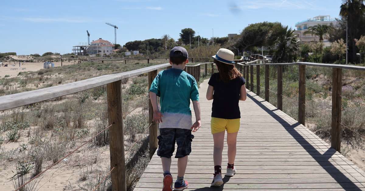 A close-up of two child siblings walking and talking together outside of the beach on the boardwalk.