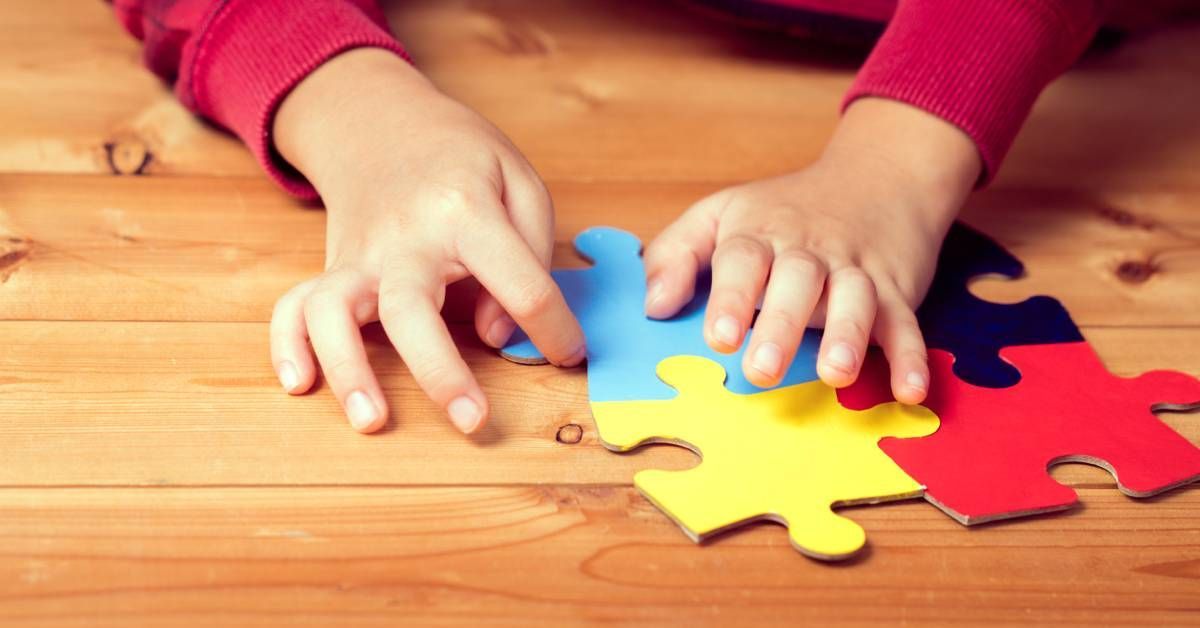 A close-up of a child's hands on four colorful puzzle pieces on a wooden floor.