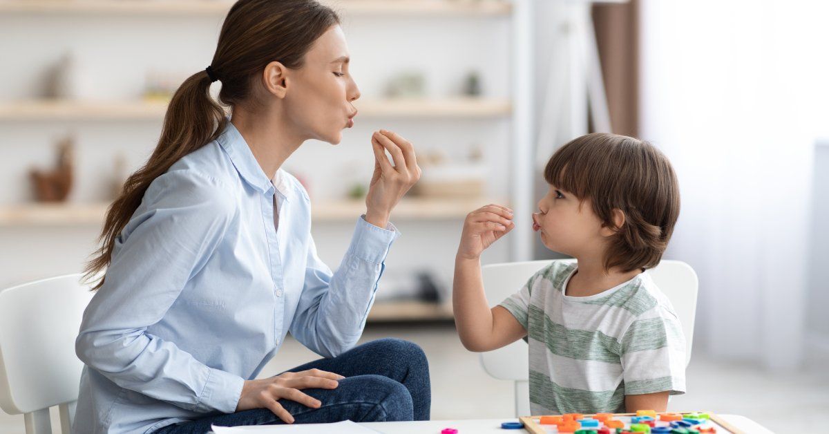 A young speech therapist and a child studying sign language together.