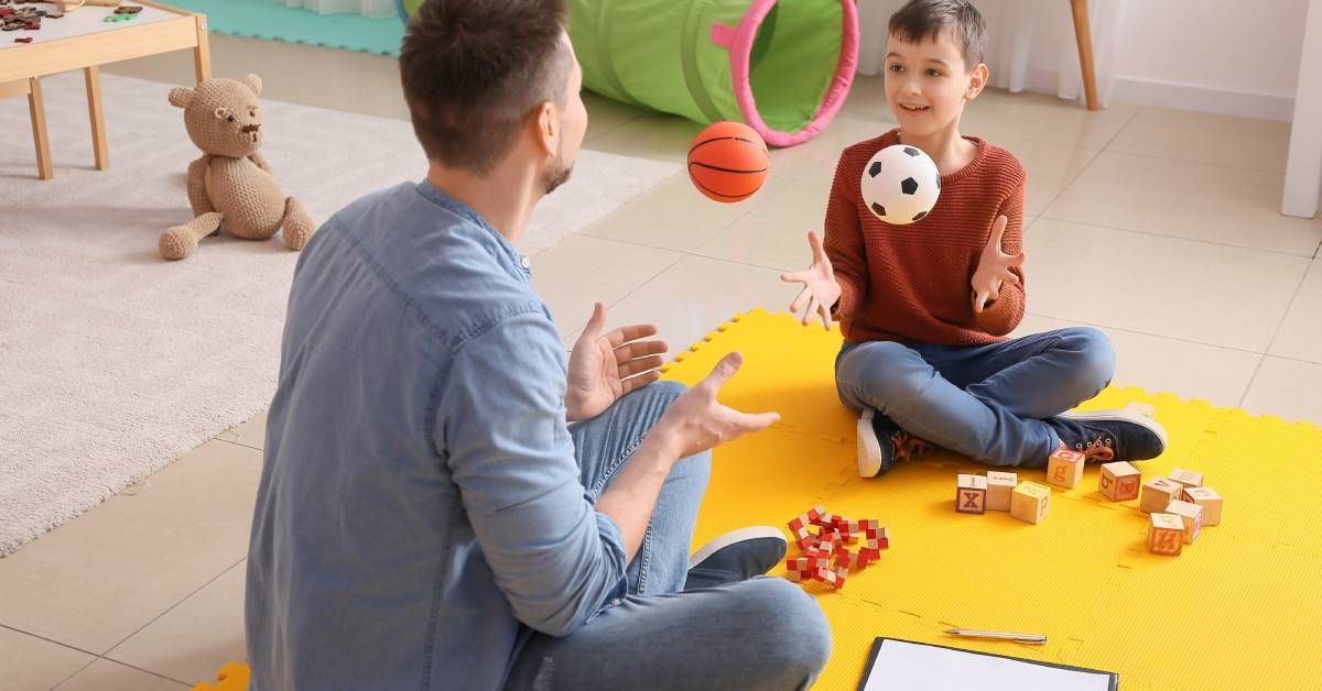 A male therapist works and plays with toys with a young boy in his office.