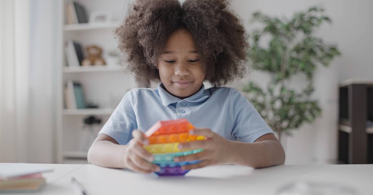 A young girl is playing with a rainbow bubble-popping fidget toy in class.