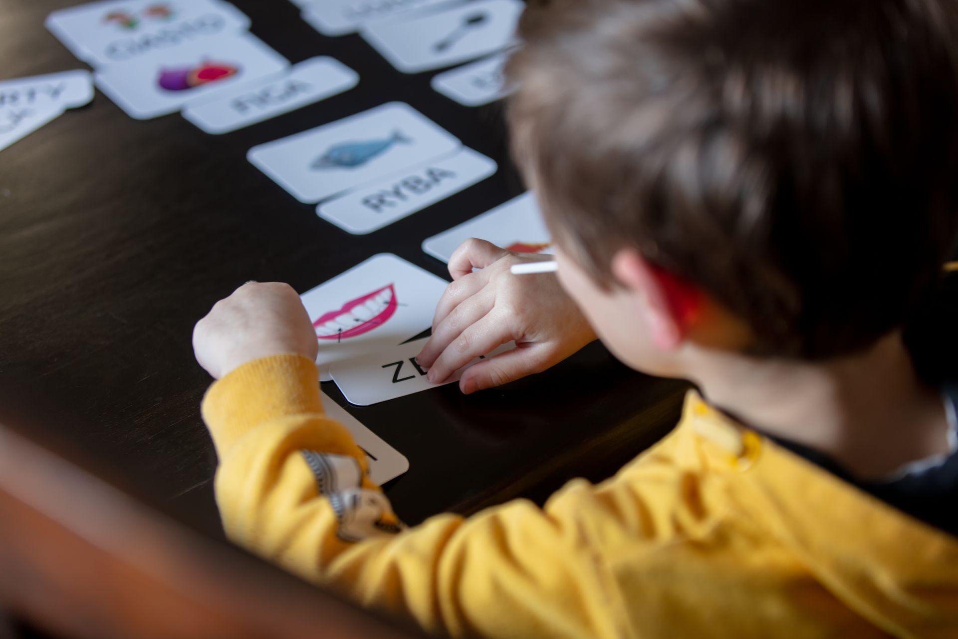 A little boy in a yellow jacket uses cards to match the corresponding word.