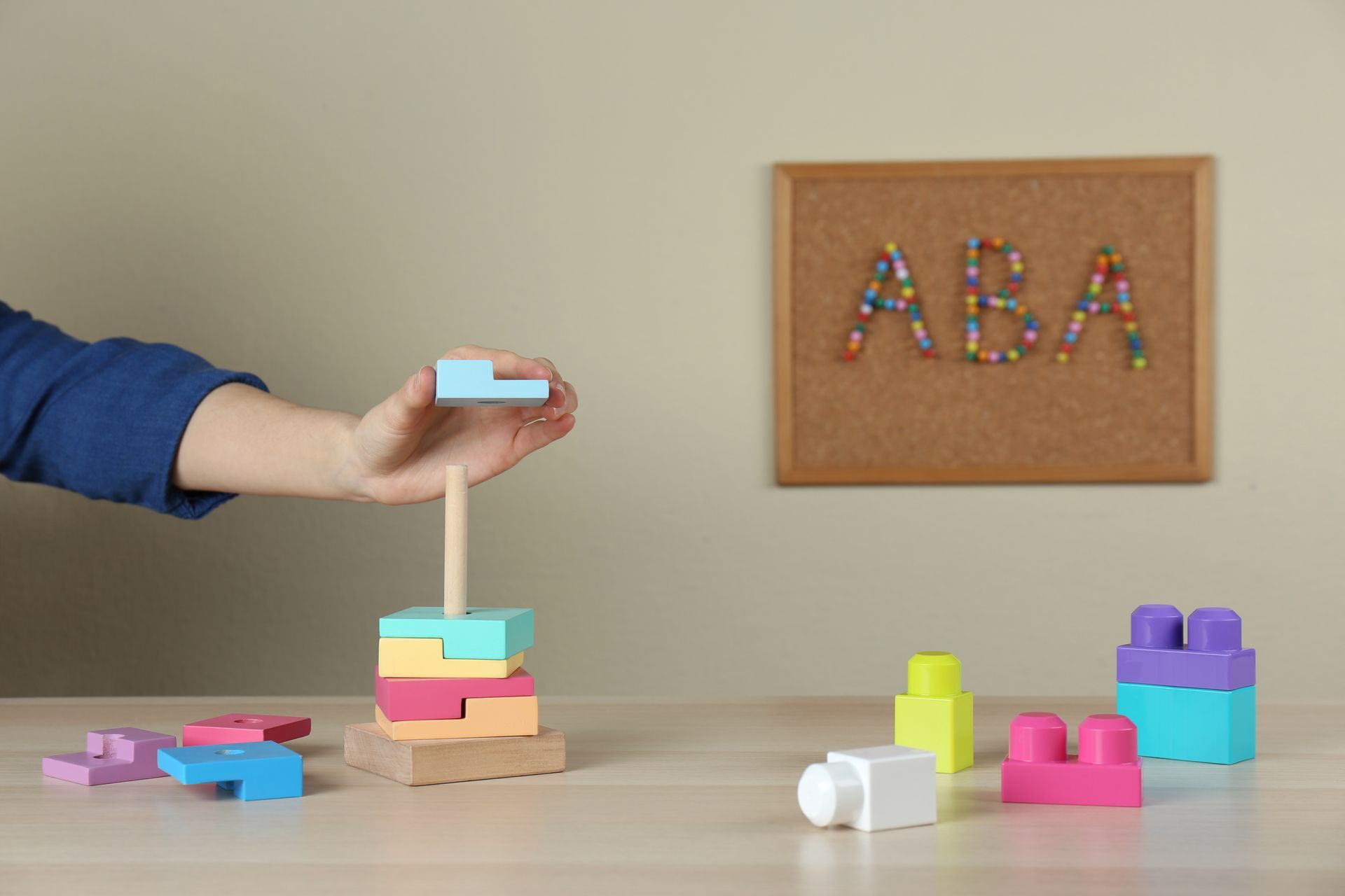 A child building a tower out of colorful wooden toys and blocks. A corkboard reads, 