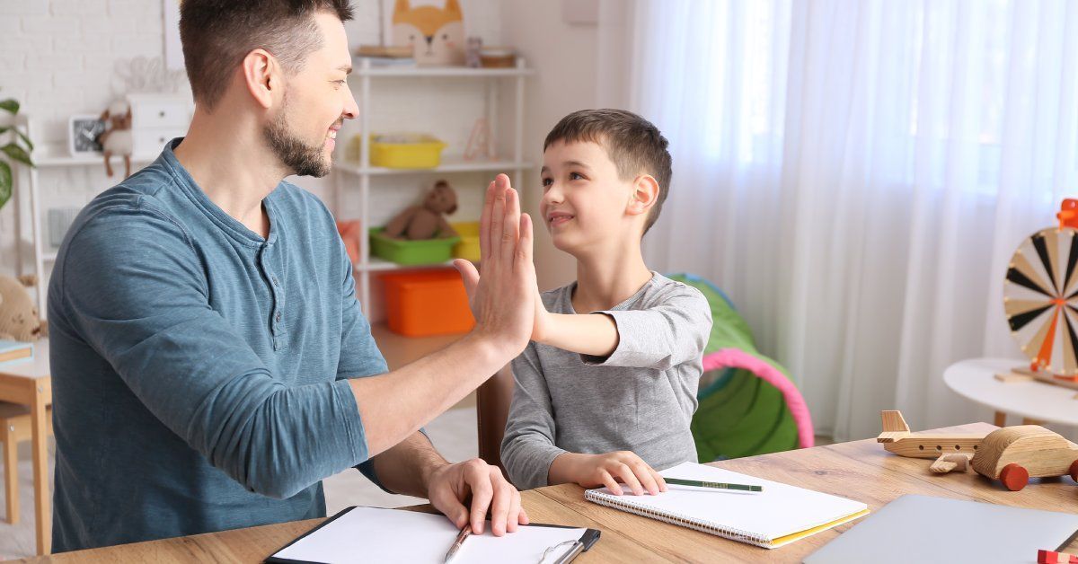 The male therapist and his student are high-fiving one another and smiling.