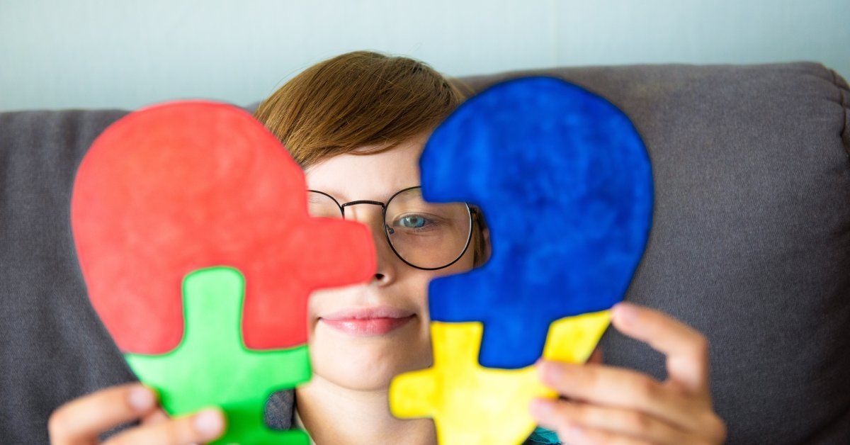 A preteen with round glasses covering his eyes with a heart puzzle piece.