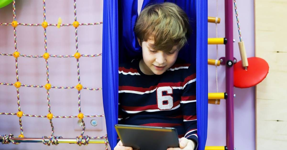 A boy is sitting on the playground while watching something on his tablet.