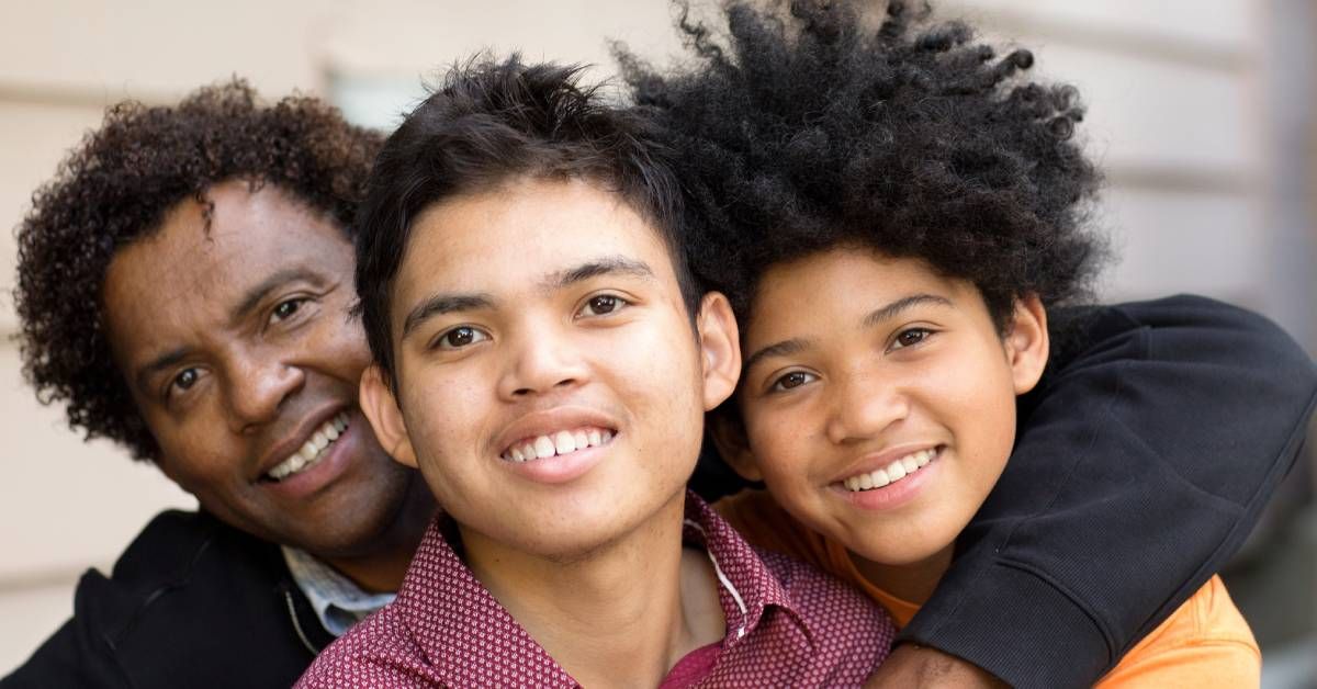 A father and his two sons hugging each other and smiling at the camera.