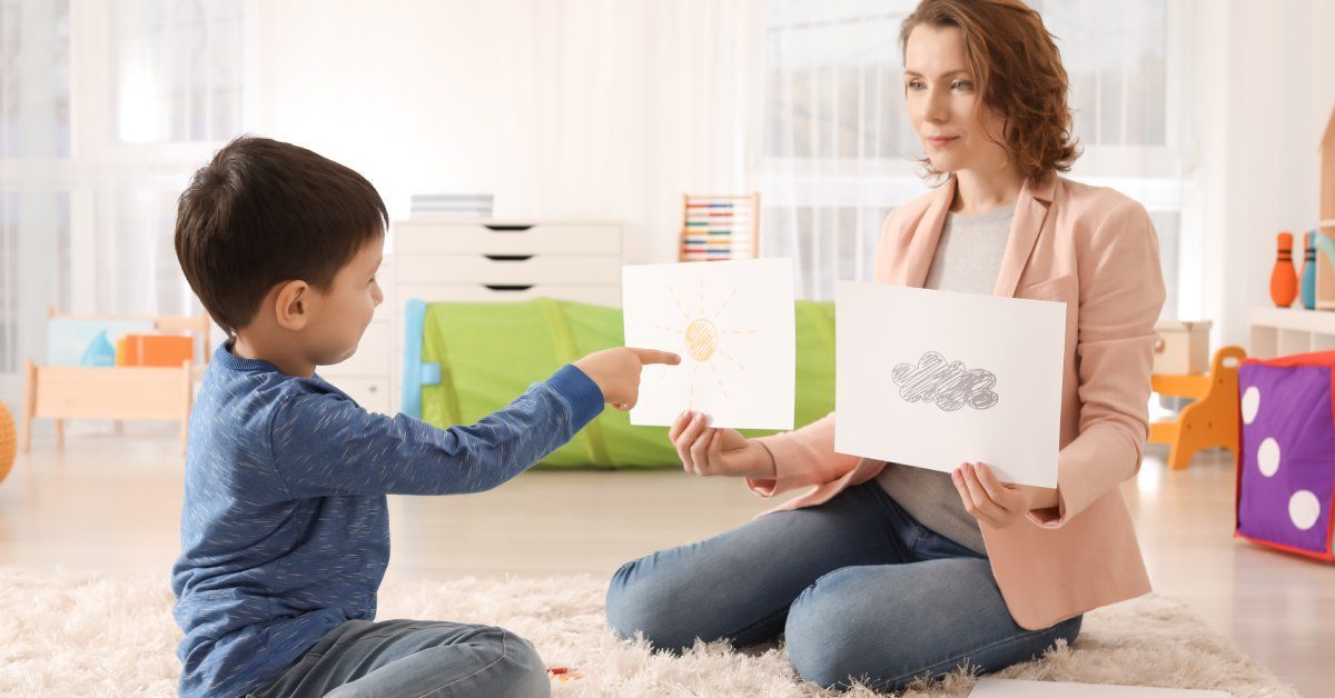 A woman holds up two pieces of paper while a child points to one. One piece of paper has the sun, and the other has a cloud.