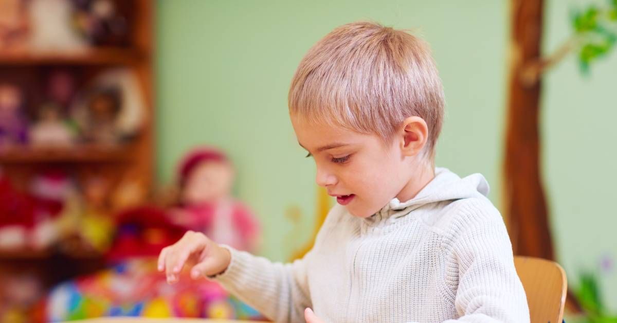 A young boy with blonde hair wearing a white sweater organizes a set of puzzle pieces, each with small red knobs.