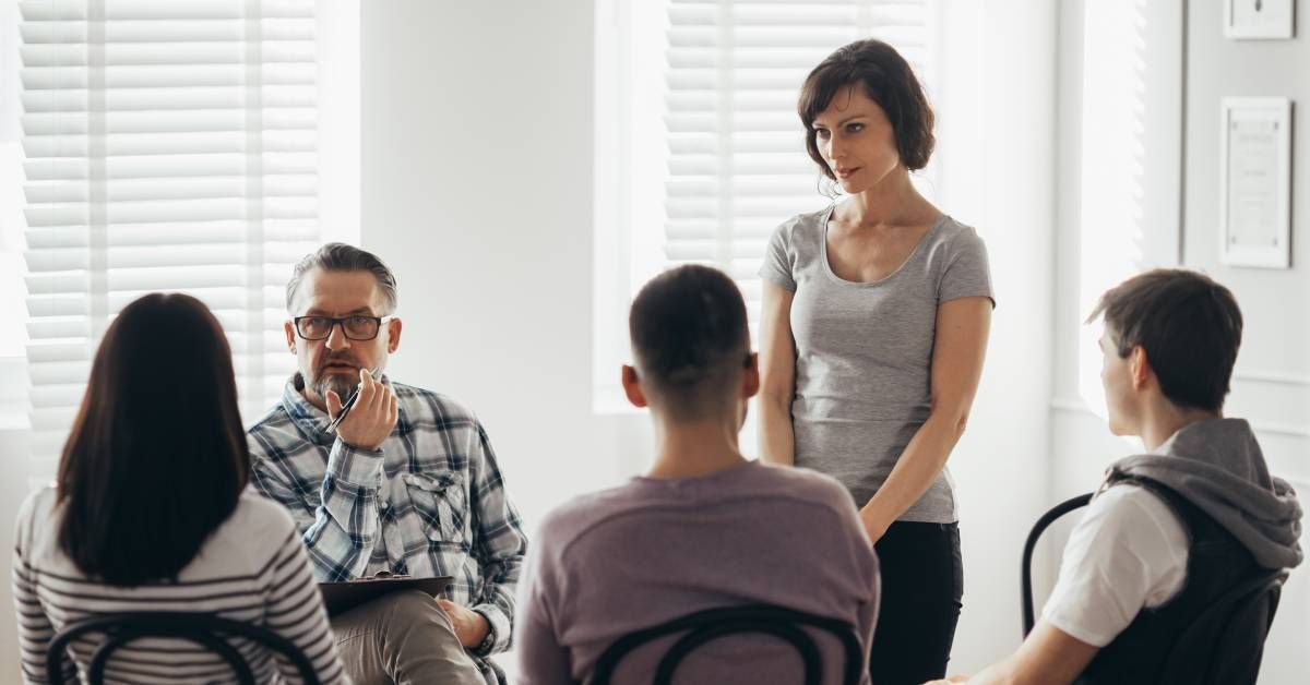 A group of people consisting of three men and two women sit together in a circle while having a discussion.