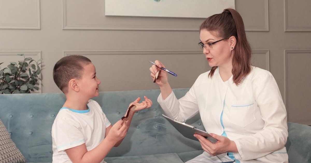 A woman wearing glasses holds a clipboard while sitting on a couch next to a little boy wearing a white T-shirt.