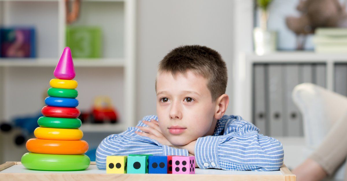 A little boy wearing a striped shirt rests his head on his arms while staring off into the distance next to puzzle pieces.