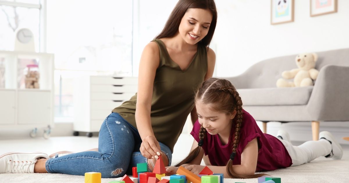 A young woman sits next to a little girl playing with colorful building blocks.