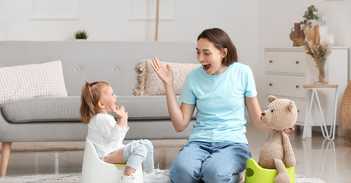 A woman smiles and gestures at a young girl who sits next to her on a small potty.