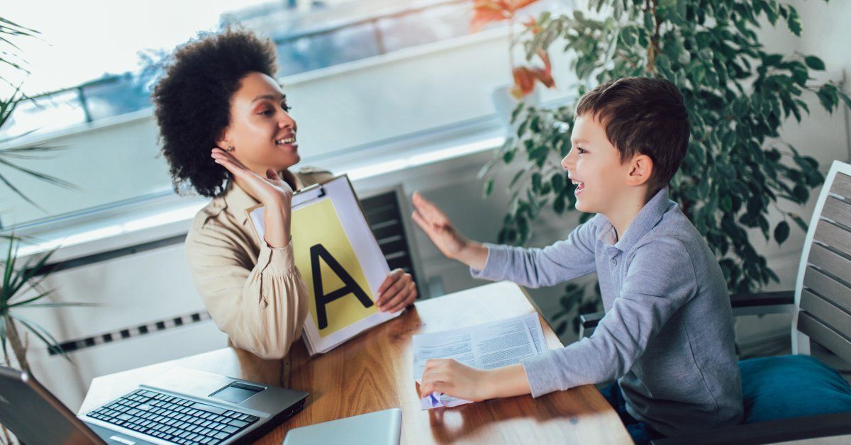 A young woman sits at a desk next to a young boy while giving him a high five.