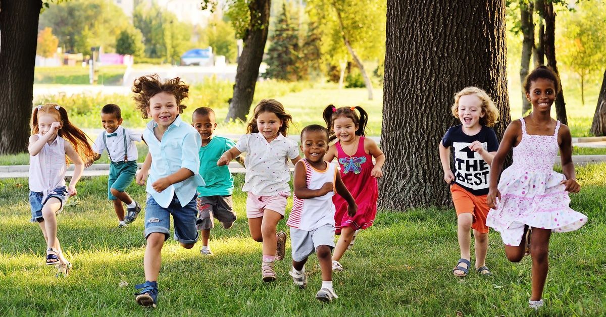 A large group of young buys and girls run past trees and through the grass.