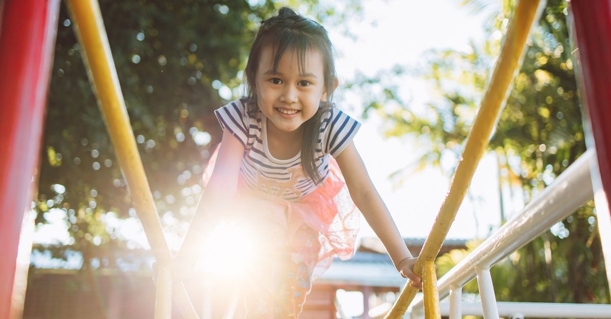 A little girl smiles while climbing on playground equipment. The child holds onto yellow bars.