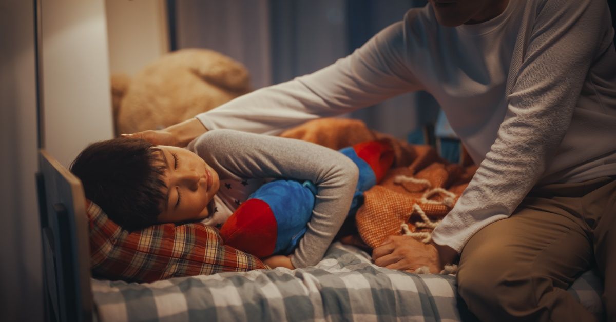 A man sitting on the edge of a bed while reaching over to comfort a child.