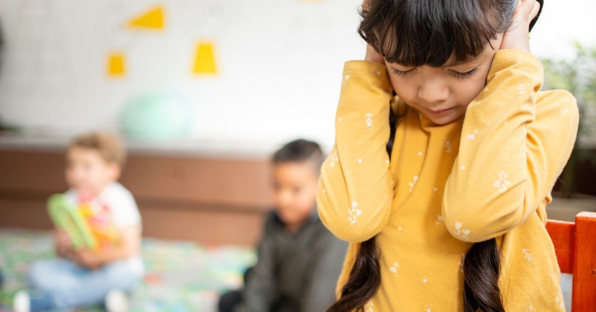 A little girl covers her ears with both hands while tightly closing her eyes.