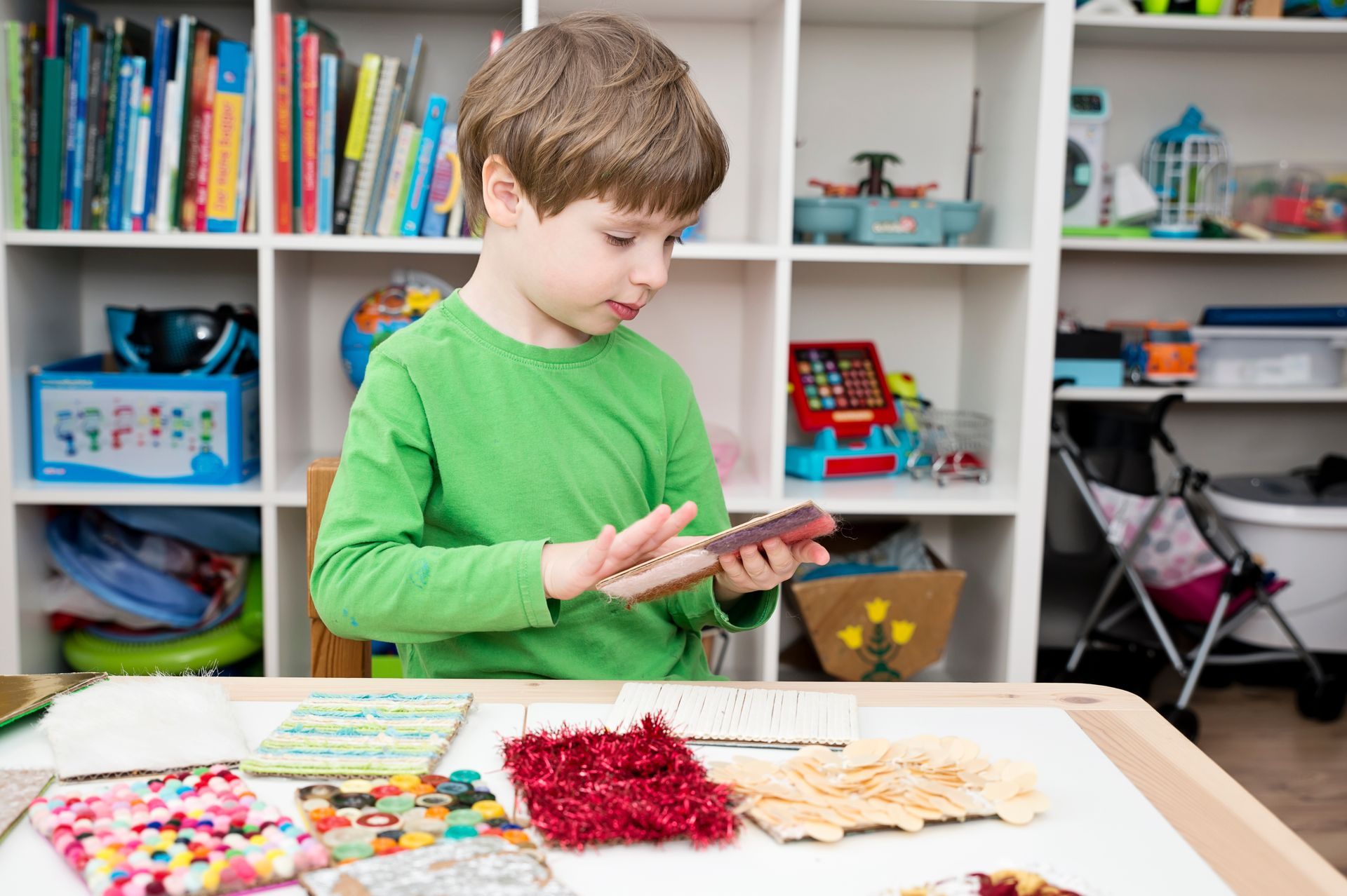 A little boy standing next to a table while touching a sensory device.