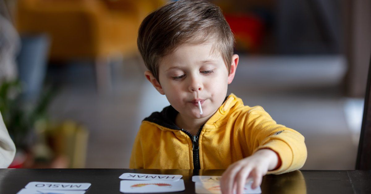 A little boy with a sucker in his mouth studies word cards at ABA therapy.