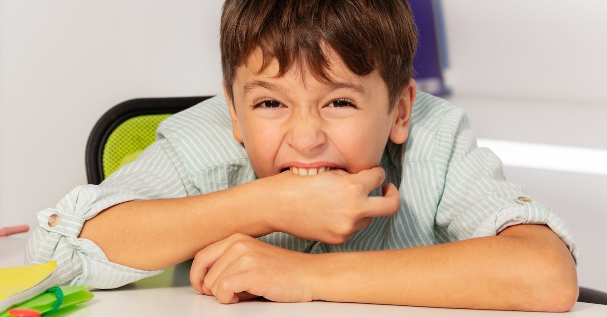 A child with autism bites his right hand during an ABA therapy session. There are number cards on the table in front of him.
