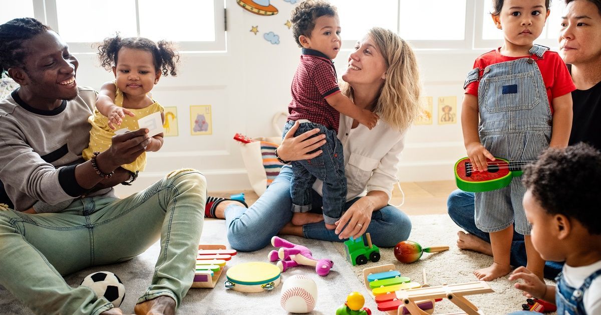 Parents and toddlers sit on the floor playing with toys in a bright classroom during an ABA therapy parent training class.