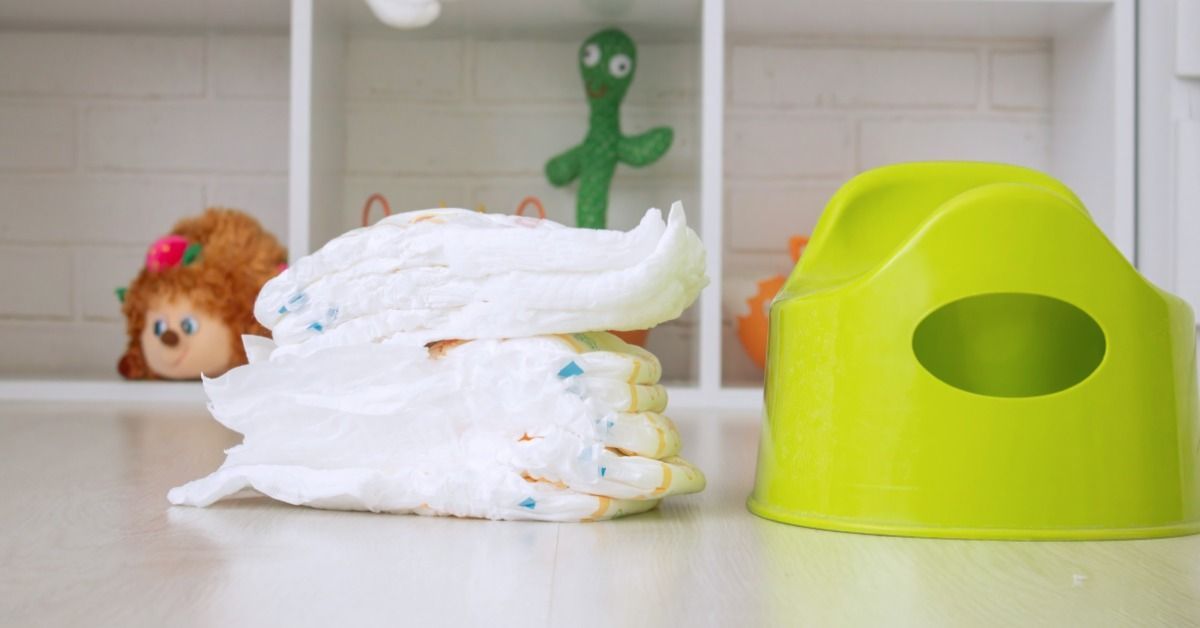 A bright green potty training seat sits beside a stack of diapers on a shelf.