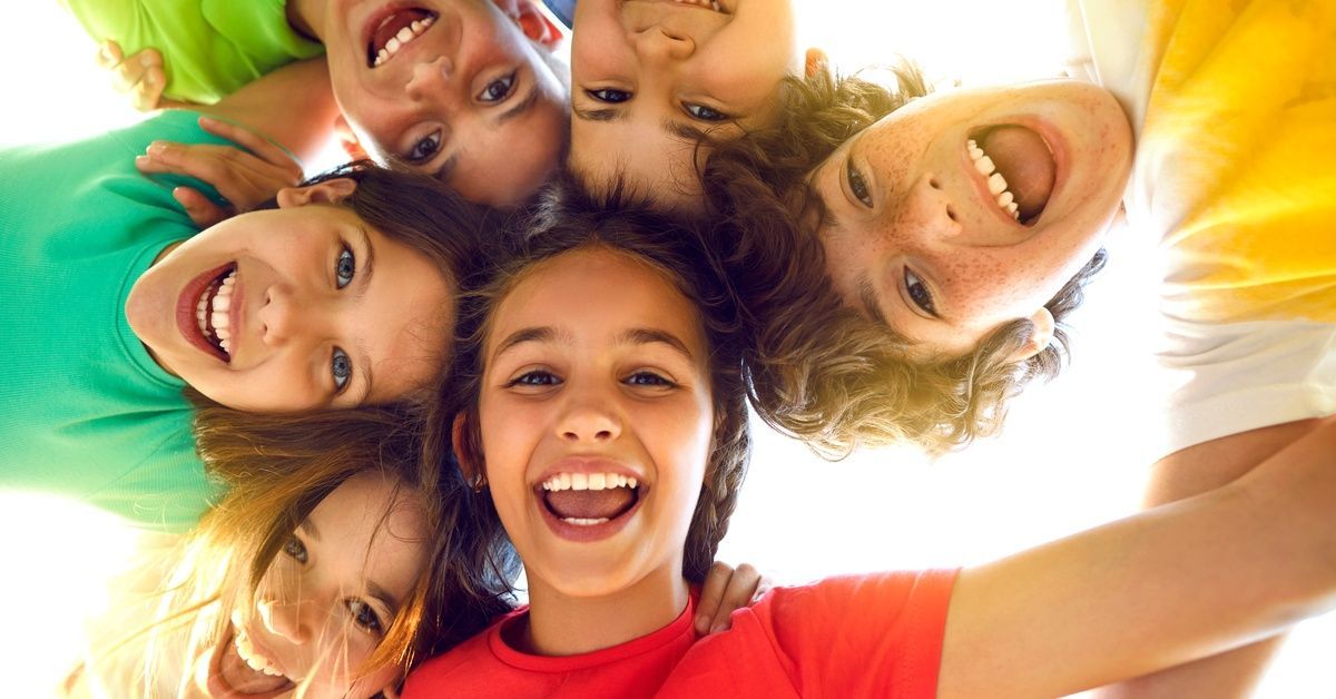 A group of happy children in colorful shirts smile brightly as their heads form a circle.