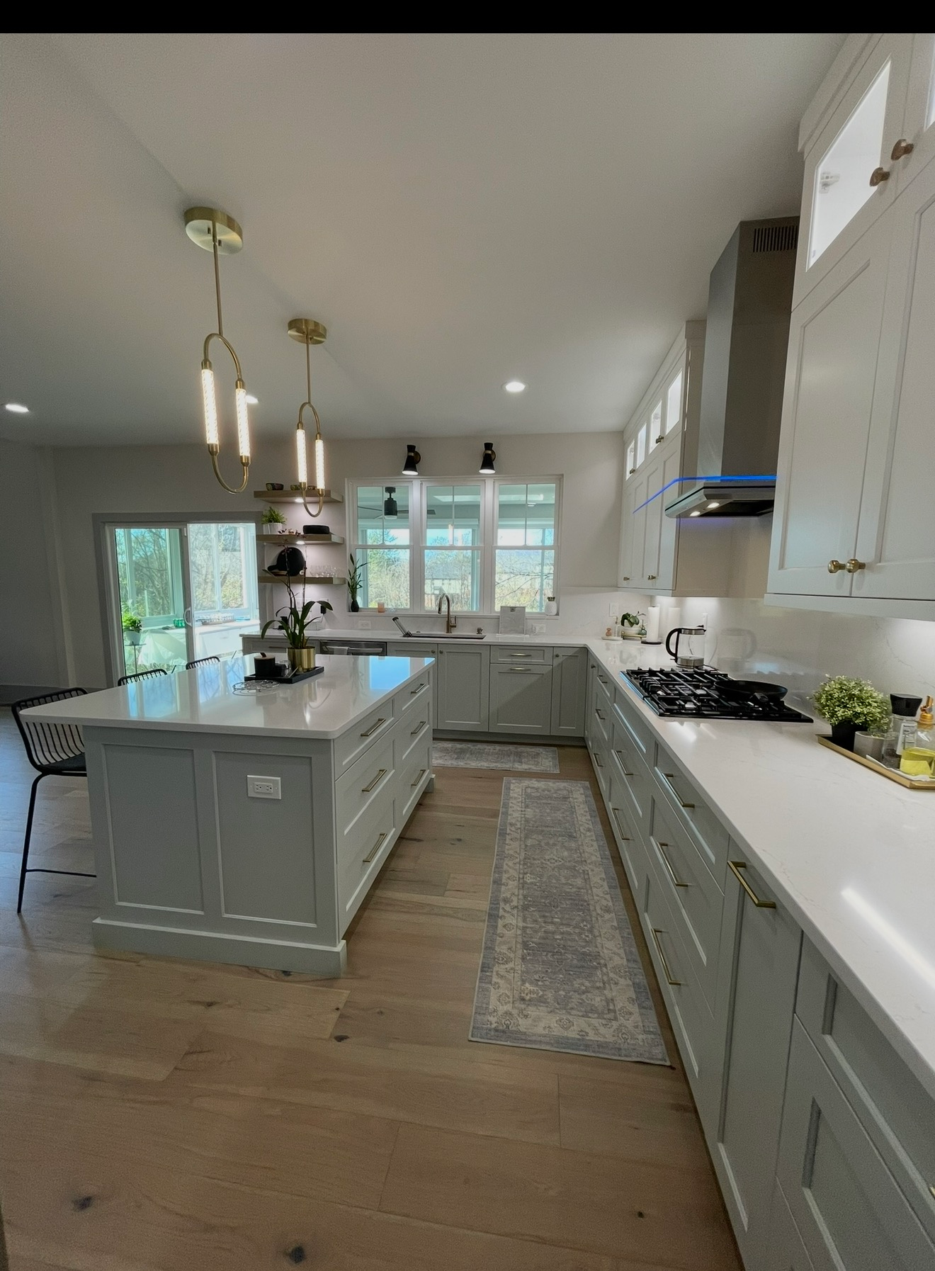 Bright modern kitchen with pale green cabinets, white countertops, island, and pendant lights.
