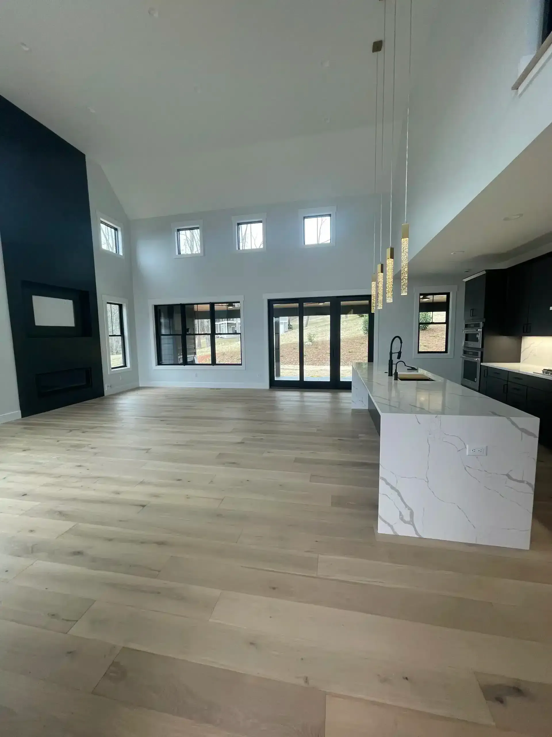 Spacious modern living room with high ceilings, light wood floors, and marble kitchen island