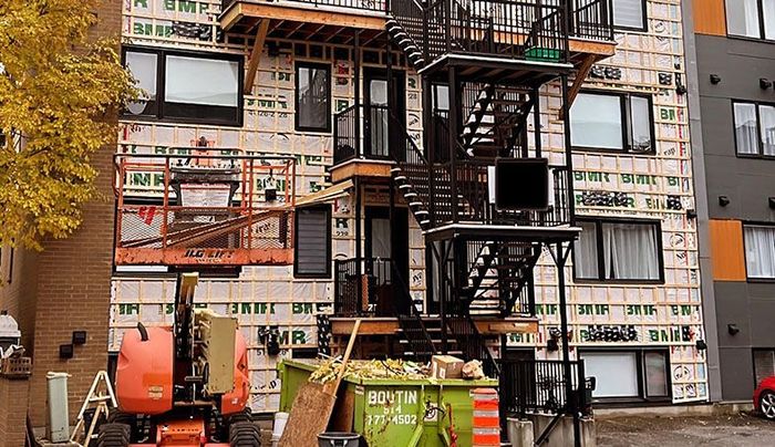 Un bâtiment en construction avec une benne verte devant.