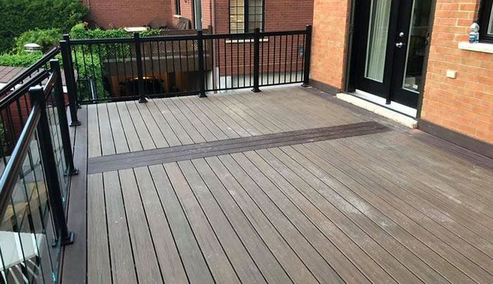 Une terrasse en bois avec une balustrade noire et un bâtiment en brique en arrière-plan.