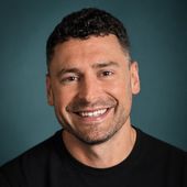 Smiling man in a black shirt against a teal studio background
